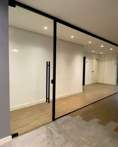 Divisória de vidro com perfil e puxador vertical pretos em ambiente interno moderno